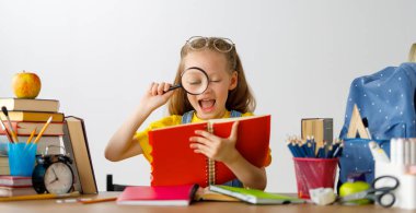 Okula dönün! Mutlu, sevimli, çalışkan çocuk kapalı bir masada oturuyor. Çocuk derste ya da derste öğreniyor.