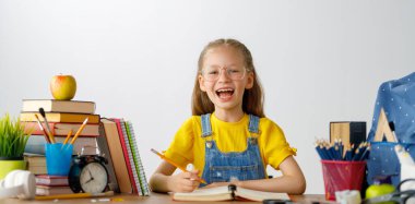 Okula dönün! Mutlu, sevimli, çalışkan çocuk kapalı bir masada oturuyor. Çocuk derste ya da derste öğreniyor.