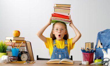 Okula dönün! Mutlu, sevimli, çalışkan çocuk kapalı bir masada oturuyor. Çocuk derste ya da derste öğreniyor.