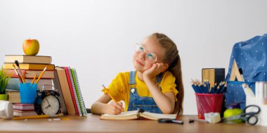 Okula dönün! Mutlu, sevimli, çalışkan çocuk kapalı bir masada oturuyor. Çocuk derste ya da derste öğreniyor.