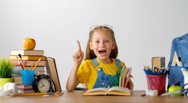 Okula dönün! Mutlu, sevimli, çalışkan çocuk kapalı bir masada oturuyor. Çocuk derste ya da derste öğreniyor.