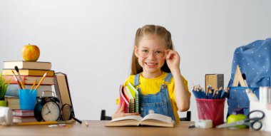 Okula dönün! Mutlu, sevimli, çalışkan çocuk kapalı bir masada oturuyor. Çocuk derste ya da derste öğreniyor.