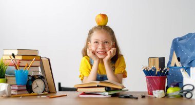 Okula dönün! Mutlu, sevimli, çalışkan çocuk kapalı bir masada oturuyor. Çocuk derste ya da derste öğreniyor.