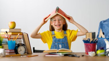 Okula dönün! Mutlu, sevimli, çalışkan çocuk kapalı bir masada oturuyor. Çocuk derste ya da derste öğreniyor.