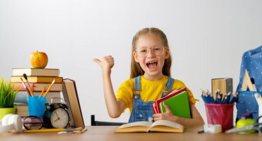 Okula dönün! Mutlu, sevimli, çalışkan çocuk kapalı bir masada oturuyor. Çocuk derste ya da derste öğreniyor.