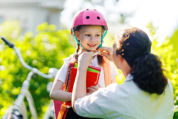Girl  in safety helmet with bike and backpack. Happy child with mother. Safe way for kids to school