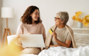 Genç ve yaşlı kadınlar online alışveriş için dizüstü bilgisayar kullanıyorlar. Kızı evde annesine yardım ediyor..