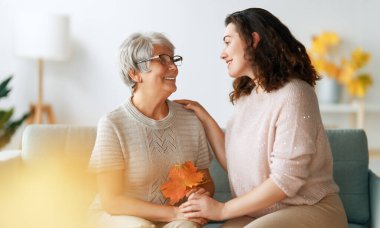 Mutlu yetişkin kadın ve kıdemli annesi, sonbahar yapraklarıyla kapalı alandalar..