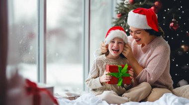 Mutlu Noeller ve mutlu tatiller. Neşeli anne ve tatlı kızı hediye değiş tokuşu yapıyor. Ebeveyn ve küçük çocuk kapalı alanda eğleniyorlar. Günaydın Xmas.. 