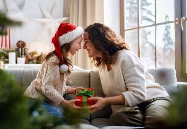 Mutlu Noeller ve mutlu tatiller. Neşeli anne ve tatlı kızı hediye değiş tokuşu yapıyor. Ebeveyn ve küçük çocuk kapalı alanda eğleniyorlar..
