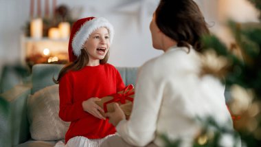 Mutlu Noeller ve mutlu tatiller. Neşeli anne ve tatlı kızı hediye değiş tokuşu yapıyor. Ebeveyn ve küçük çocuk kapalı alanda eğleniyorlar..