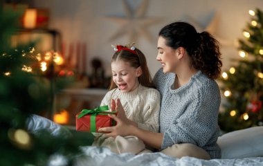 Mutlu Noeller ve mutlu tatiller. Neşeli anne ve tatlı kızı hediye değiş tokuşu yapıyor. Ebeveyn ve küçük çocuk kapalı alanda eğleniyorlar. Odasında hediyeler olan sevgi dolu bir aile.                               