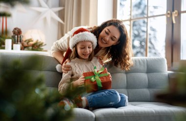 Mutlu Noeller ve mutlu tatiller. Neşeli anne ve tatlı kızı hediye değiş tokuşu yapıyor. Ebeveyn ve küçük çocuk kapalı alanda eğleniyorlar..