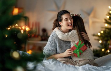 Mutlu Noeller ve mutlu tatiller. Neşeli anne ve tatlı kızı hediye değiş tokuşu yapıyor. Ebeveyn ve küçük çocuk kapalı alanda eğleniyorlar. Odasında hediyeler olan sevgi dolu bir aile.