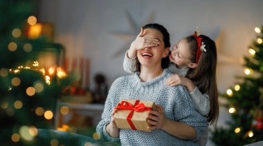 Mutlu Noeller ve mutlu tatiller. Neşeli anne ve tatlı kızı hediye değiş tokuşu yapıyor. Ebeveyn ve küçük çocuk kapalı alanda eğleniyorlar. Odasında hediyeler olan sevgi dolu bir aile.
