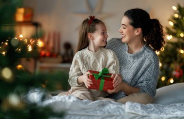 Mutlu Noeller ve mutlu tatiller. Neşeli anne ve tatlı kızı hediye değiş tokuşu yapıyor. Ebeveyn ve küçük çocuk kapalı alanda eğleniyorlar. Odasında hediyeler olan sevgi dolu bir aile.