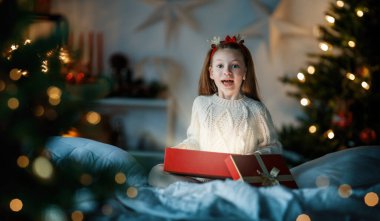 Mutlu Noeller ve mutlu tatiller. Hediyesi olan neşeli, sevimli bir kız çocuğu. Çocuk ağacın yanında eğleniyor..    