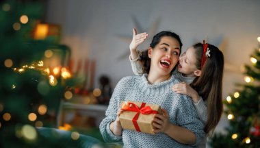 Mutlu Noeller ve mutlu tatiller. Neşeli anne ve tatlı kızı hediye değiş tokuşu yapıyor. Ebeveyn ve küçük çocuk kapalı alanda eğleniyorlar. Odasında hediyeler olan sevgi dolu bir aile.