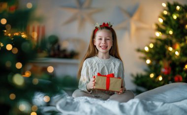 Mutlu Noeller ve mutlu tatiller. Hediyesi olan neşeli, sevimli bir kız çocuğu. Çocuk ağacın yanında eğleniyor..    