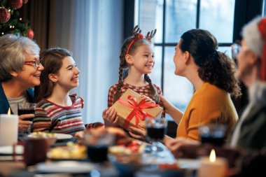  Mutlu Noeller! Mutlu aile evde yemek yiyor. Kutlama tatili ve ağacın yakınındaki birliktelik.