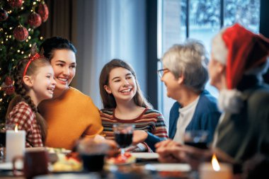 Mutlu Noeller! Mutlu aile evde yemek yiyor. Kutlama tatili ve ağacın yakınındaki birliktelik.