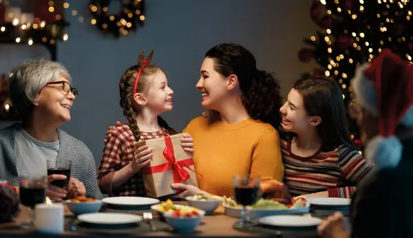  Mutlu Noeller! Mutlu aile evde yemek yiyor. Kutlama tatili ve ağacın yakınındaki birliktelik.