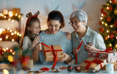 İyi tatiller. Neşeli büyükanne, anne ve tatlı kız Noel için hazırlanıyor. İnsanlar hediyeleri paketliyor, evi dekore ediyor. Odasında hediyeler olan sevgi dolu bir aile.