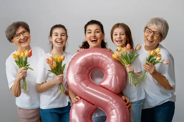 Happy women\'s day! Children daughters are congratulating mom and grandmothers giving them flowers tulips. Grannys, mom and girls smiling on light grey background. Family holiday and togetherness.