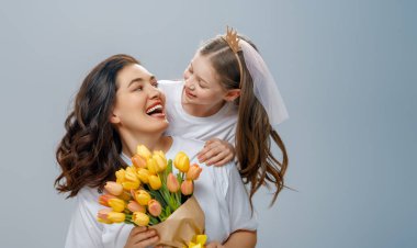 Mutlu kadınlar günü. Çocuk annemi tebrik ediyor ve ona sarı çiçekler veriyor. Anne ve kız açık gri arka planda gülümsüyor. Aile tatili ve birliktelik. 