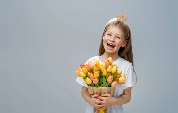 Beautiful girl with yellow flowers in hands on grey wall background.