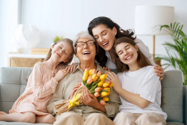 ハッピーマザーの日 子供の娘と母親は 彼女の花チューリップを与えるおばあちゃんを祝福しています おばあちゃん お母さん 女の子たちは笑顔で抱きしめています 家族の休日とトータル — ストック写真