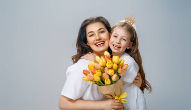 Mutlu kadınlar günü. Çocuk annemi tebrik ediyor ve ona sarı çiçekler veriyor. Anne ve kız açık gri arka planda gülümsüyor. Aile tatili ve birliktelik. 