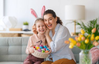 İyi tatiller! Anne ve kızı yumurta boyuyor. Paskalyayı kutlayan aile. Sevimli küçük kız tavşan kulağı takıyor..