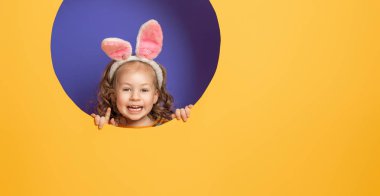 Paskalya günü tavşan kulağı takan şirin bir çocuk. Parlak mor ve sarı arka planda bir kız. 