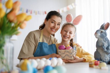 Anne ve kızı yumurta boyuyor. Mutlu aile Paskalya için hazırlanıyor. Tavşan kulağı takan şirin bir kız çocuğu..