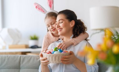 İyi tatiller! Anne ve kızı yumurta boyuyor. Paskalyayı kutlayan aile. Sevimli küçük kız tavşan kulağı takıyor..