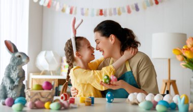 Anne ve kızı yumurta boyuyor. Mutlu aile Paskalya için hazırlanıyor. Tavşan kulağı takan şirin bir kız çocuğu..