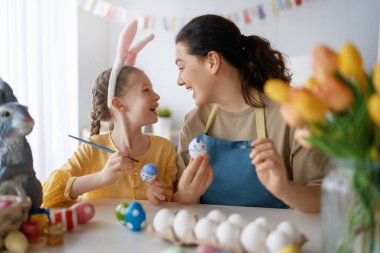 Anne ve kızı yumurta boyuyor. Mutlu aile Paskalya için hazırlanıyor. Tavşan kulağı takan şirin bir kız çocuğu..