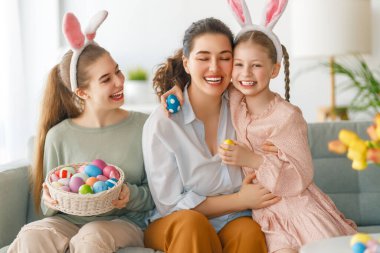 İyi tatiller. Anne ve kızları yumurta boyuyor. Paskalyayı kutlayan aile. Sevimli küçük çocuklar tavşan kulağı takıyor.. 