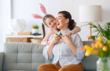 İyi tatiller! Anne ve kızı yumurta boyuyor. Paskalyayı kutlayan aile. Sevimli küçük kız tavşan kulağı takıyor..
