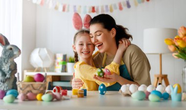 Anne ve kızı yumurta boyuyor. Mutlu aile Paskalya için hazırlanıyor. Tavşan kulağı takan şirin bir kız çocuğu..