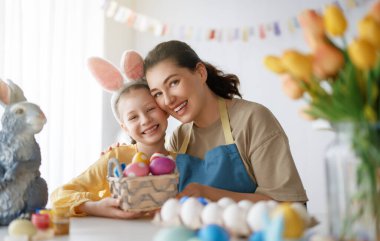 Anne ve kızı yumurta boyuyor. Mutlu aile Paskalya için hazırlanıyor. Tavşan kulağı takan şirin bir kız çocuğu..