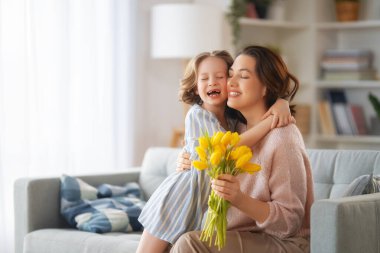 Anneler Günün kutlu olsun. Çocuk kızı annemi tebrik ediyor ve ona çiçek veriyor. Anne ve kız gülümsüyor ve sarılıyorlar. Aile tatili ve birliktelik.