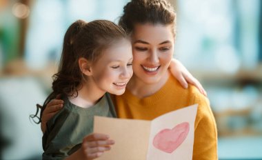Anneler Günün kutlu olsun. Çocuk kızı annemi tebrik ediyor ve ona kartpostal veriyor. Anne ve kız gülümsüyor ve sarılıyorlar. Aile tatili ve birliktelik.