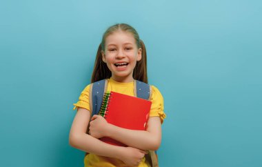 Açık mavi arka planda duran sevimli mutlu çocuk. Sırt çantalı çocuk, küçük kız okula dönmeye hazır.. 