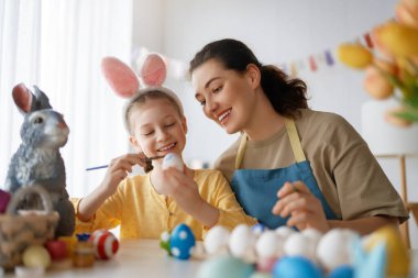 Anne ve kızı yumurta boyuyor. Mutlu aile Paskalya için hazırlanıyor. Tavşan kulağı takan şirin bir kız çocuğu..