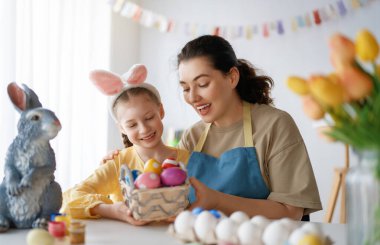 Anne ve kızı yumurta boyuyor. Mutlu aile Paskalya için hazırlanıyor. Tavşan kulağı takan şirin bir kız çocuğu..
