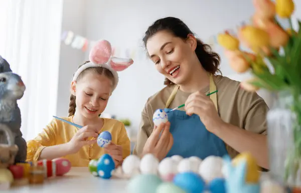 妈妈和她的女儿画鸡蛋 快乐的家庭为复活节做准备 可爱的小女孩 长着小兔子耳朵 — 图库照片