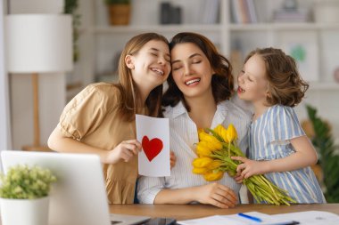 Anneler Günün kutlu olsun. Çocuklar annelerini tebrik ediyor ve ona çiçek veriyorlar. Anne ve kızlar gülümsüyor ve sarılıyorlar. Aile tatili ve birliktelik.