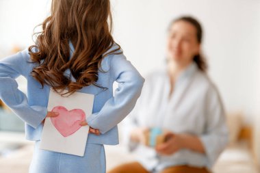 Anneler Günün kutlu olsun. Çocuk kızı annemi tebrik ediyor ve ona kartpostal veriyor. Anne ve kız gülümsüyor ve sarılıyorlar. Aile tatili ve birliktelik.